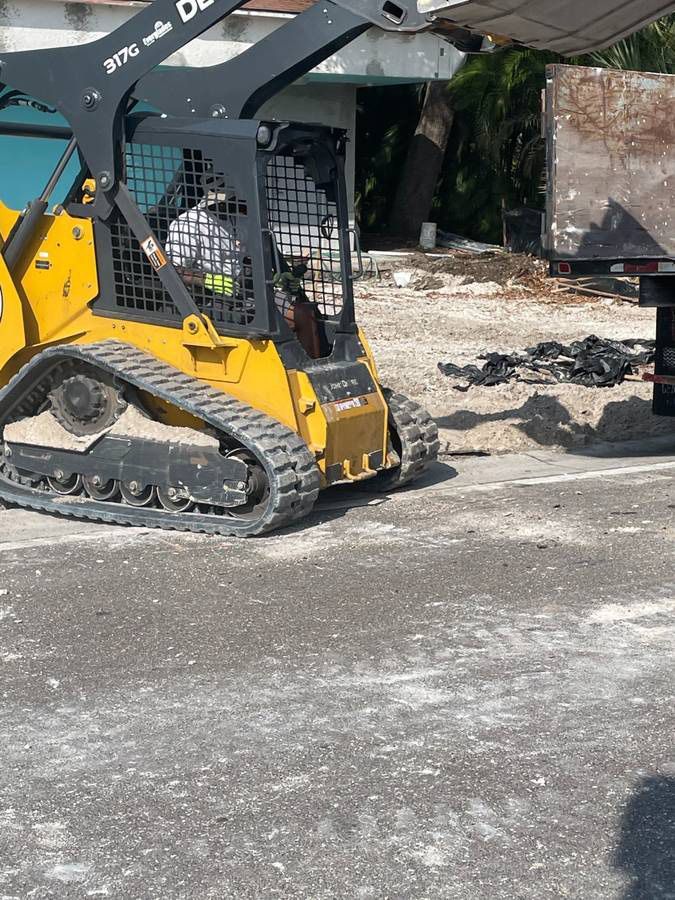 Yellow Deere skid steer loading debris onto a trailer in an outdoor setting.