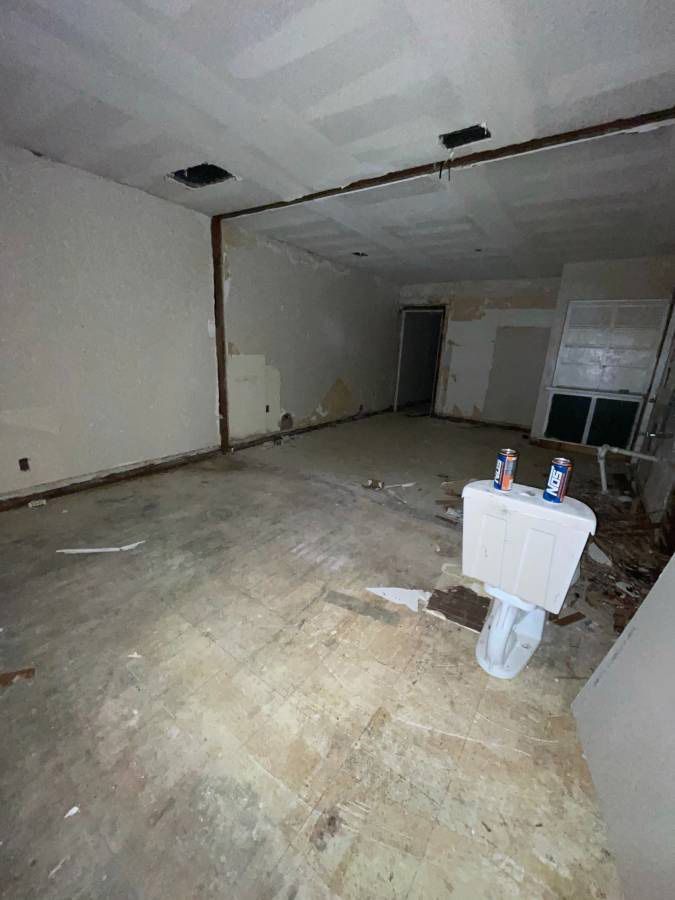 Empty room under renovation; exposed ceiling, walls, and flooring; debris scattered.
