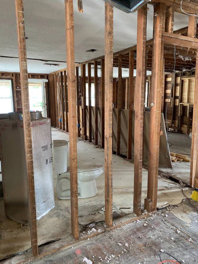 Interior house demolition showing exposed studs, toilet, and debris on the floor.