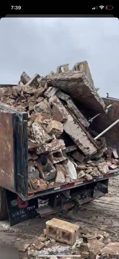 A truck bed overflowing with construction debris: concrete, bricks, and blocks. Overcast sky.