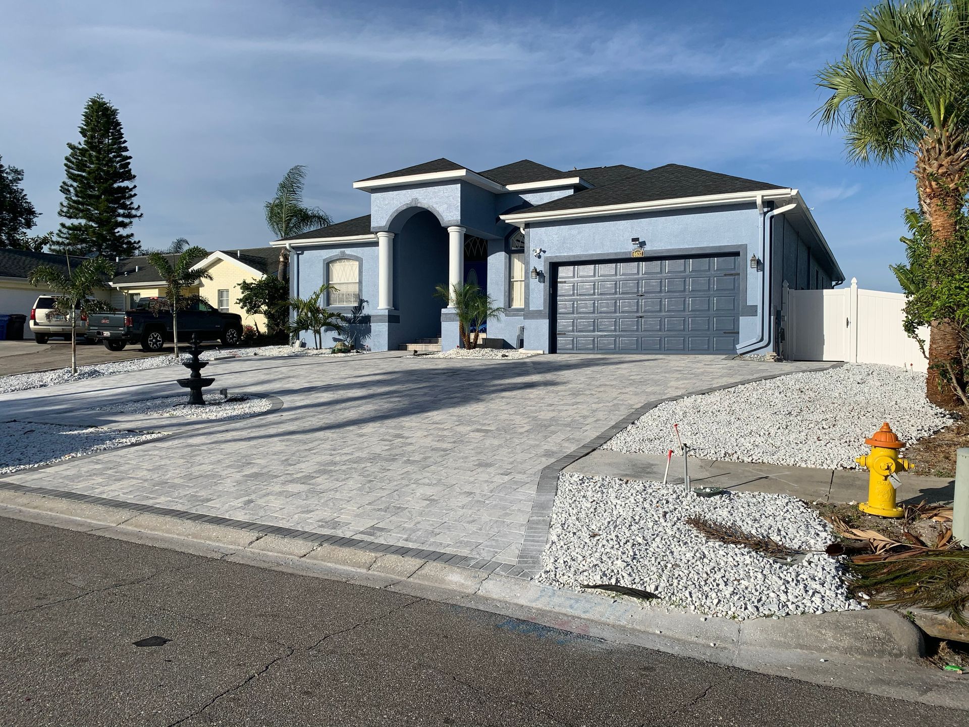 Blue house with white gravel driveway, palm tree, and blue sky.