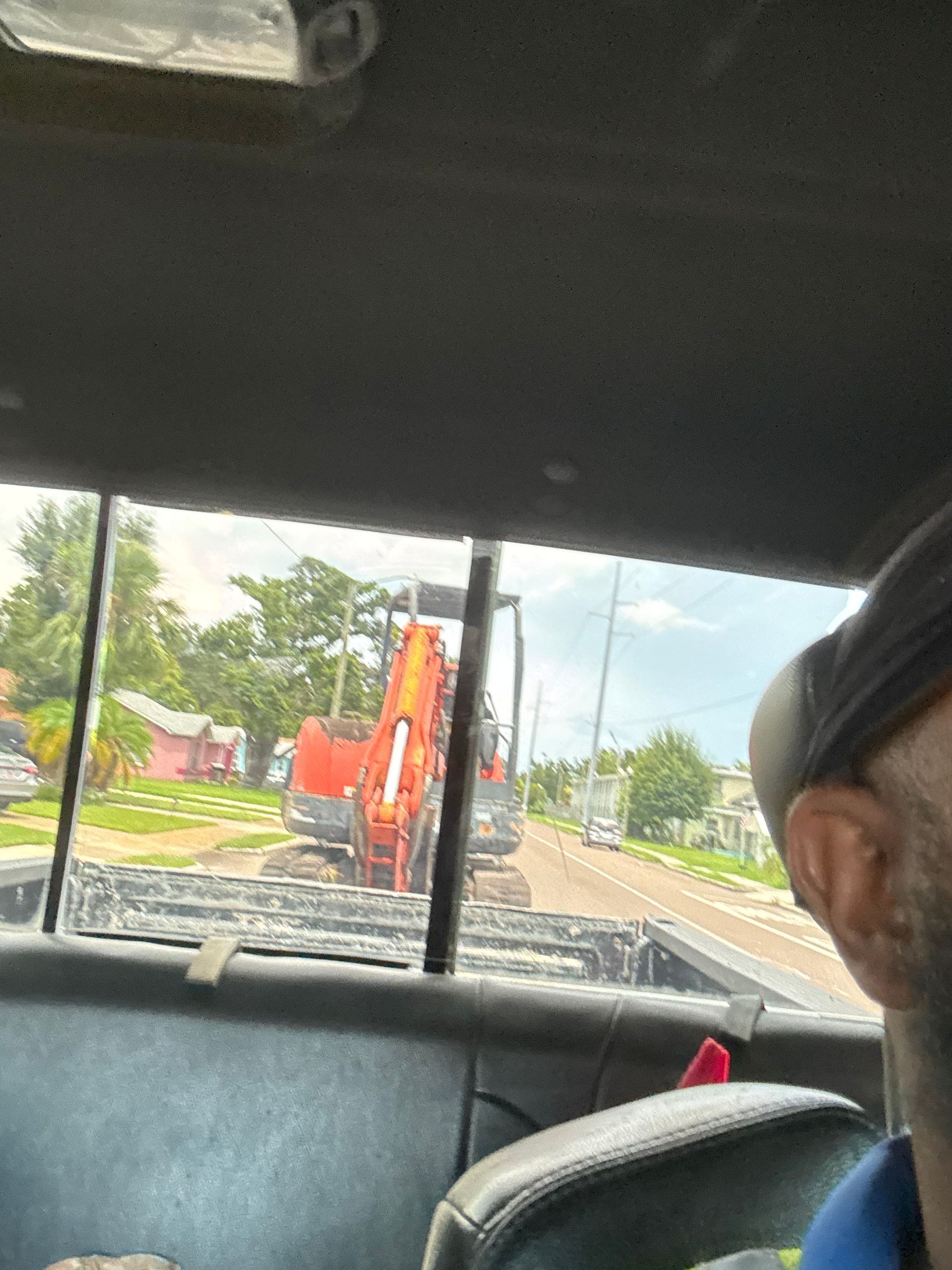 An orange excavator is being transported on a trailer down a residential street.