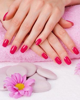 Hands with bright pink nail polish, resting on a pink towel, with stones and a pink flower.