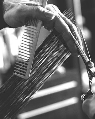 Hand holding comb and scissors cutting hair.