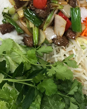 Close-up of a plate with stir-fried beef and vegetables, herbs, bean sprouts, and carrots.