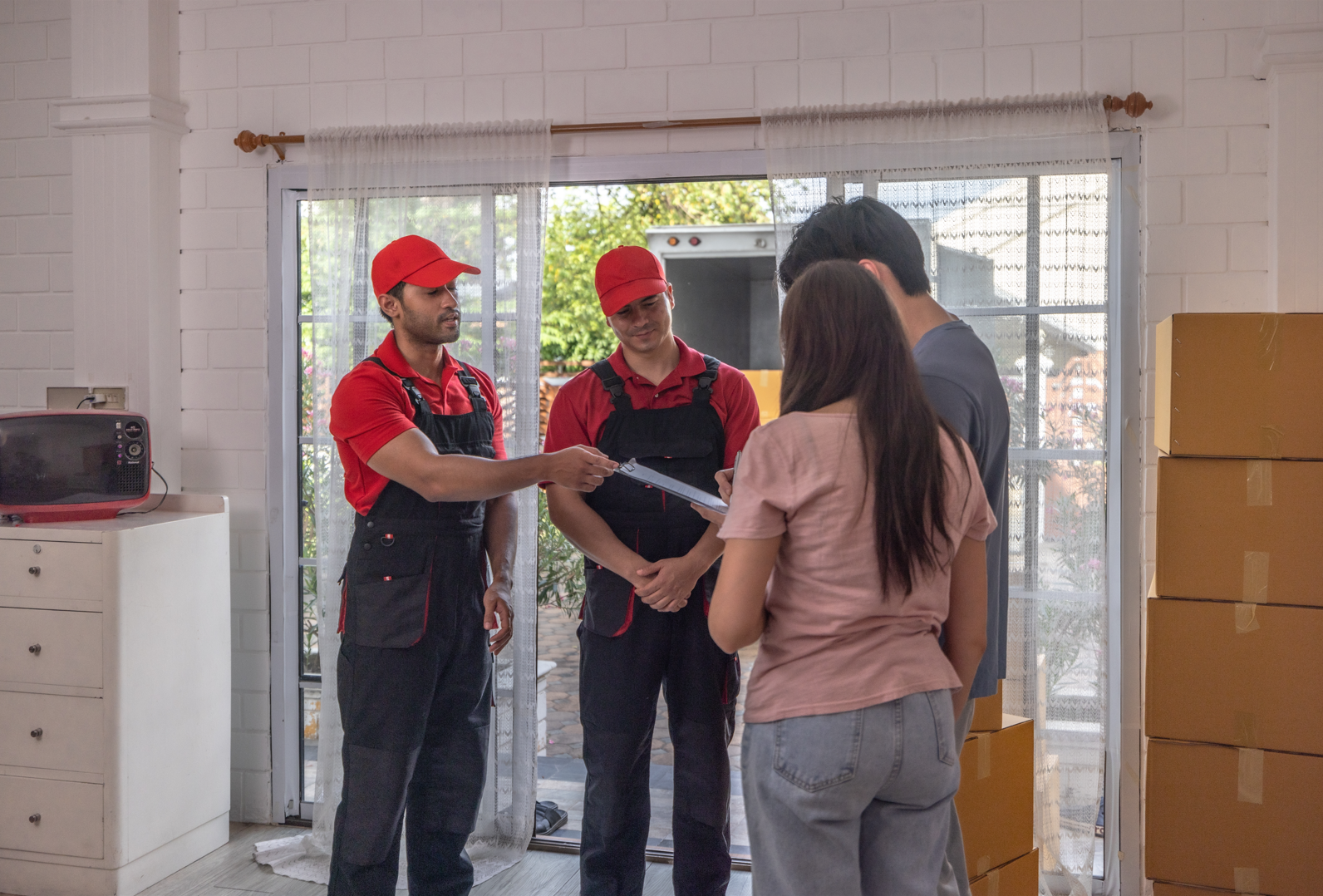 A group of movers are standing next to a woman in a living room.