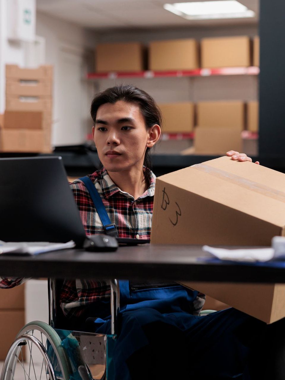 A man in a wheelchair is sitting at a desk holding a cardboard box.