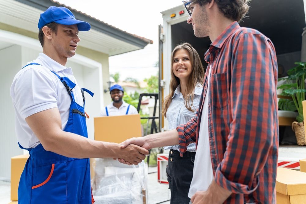 A man is shaking hands with a man and woman in front of a moving truck.