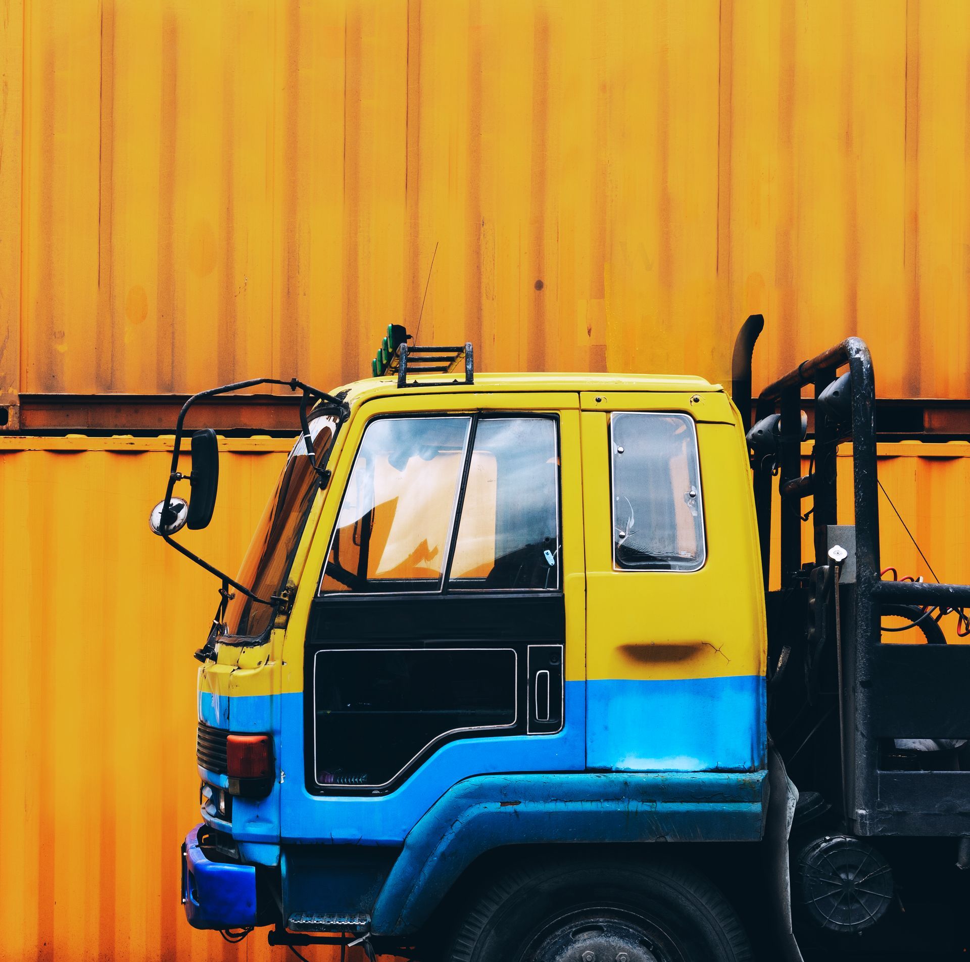 A yellow and blue truck is parked in front of an orange container