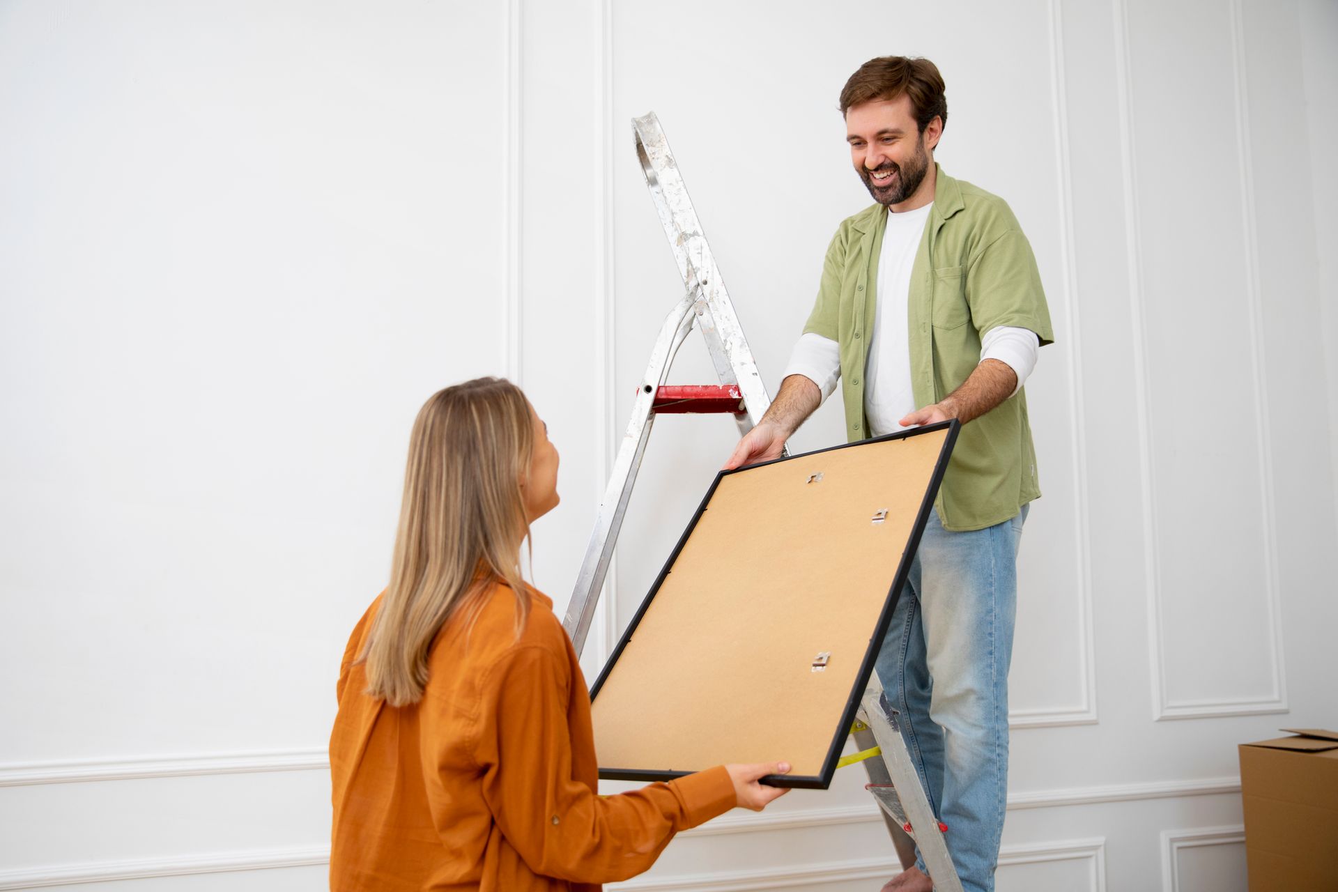 A man and a woman are hanging a picture on a wall.