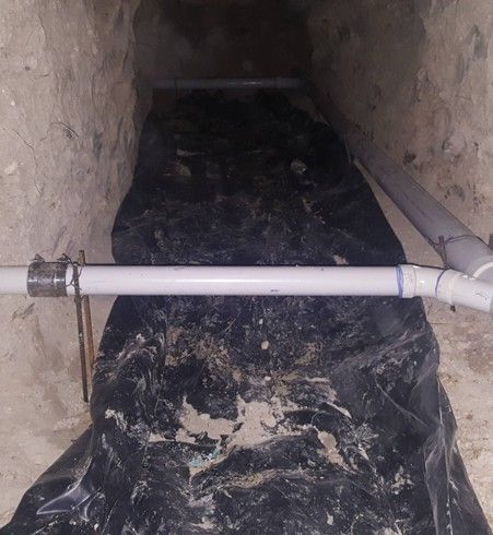 Trench with black plastic sheeting and PVC pipes. Dark, interior setting.