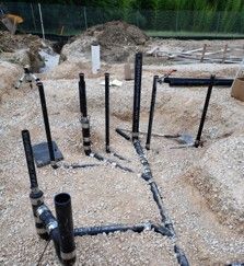Black plumbing pipes set in gravel at a construction site.