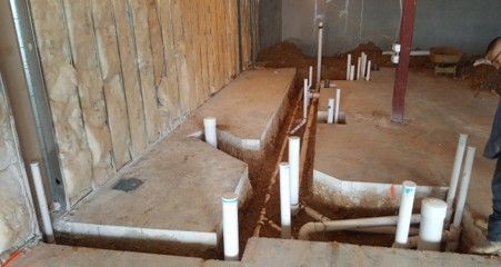 Interior construction site with white PVC pipes and trenches in a concrete floor.