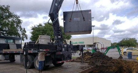A crane lifts a large, dark box over a construction site near a Dollar Tree store.