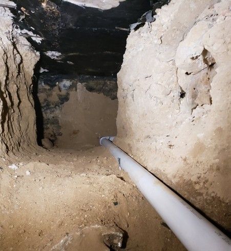 Narrow, earthen tunnel with a white pipe extending into the darkness.