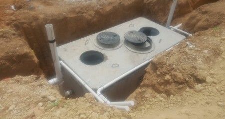 Concrete septic tank in a dirt trench with PVC pipes connected.
