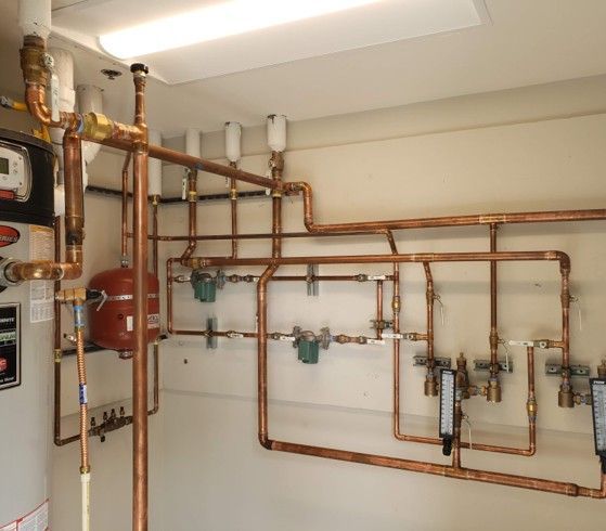 Copper pipes and various components for a water heating system installed on a light-colored wall.