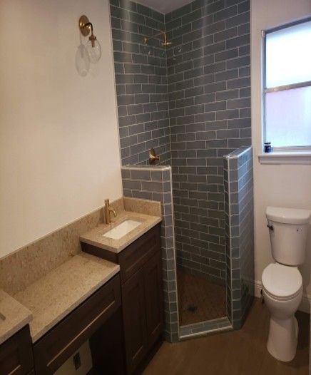 Bathroom with a tiled shower, gold fixtures, dark cabinets, and a white toilet.