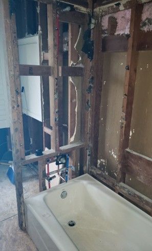 A bathroom undergoing renovation, tub installed, exposed wood studs, water pipes visible.