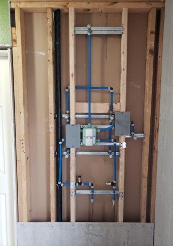 Framed-in plumbing with blue pipes, a shower valve, and metal supports.