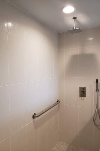 Shower stall with light-colored tiles, overhead showerhead, grab bar, and control panel.
