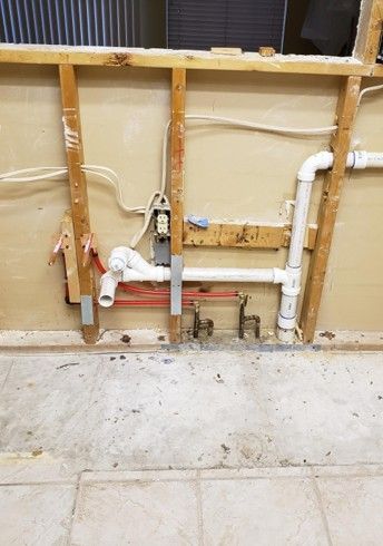 Exposed plumbing and electrical wiring in a wall cavity during renovation. Red and white pipes, wooden framing.