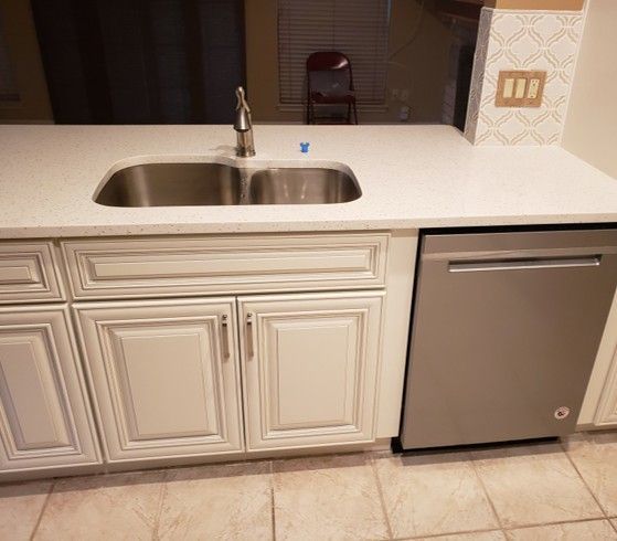 White kitchen cabinets with a double sink, countertop, and a stainless steel dishwasher.