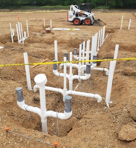 Excavation site with white PVC pipes for plumbing, a small bulldozer, and safety tape.