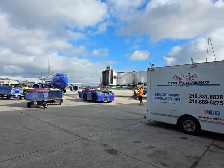 An airport scene with a Southwest plane, vehicles, and a COR Plumbing van on a sunny day.