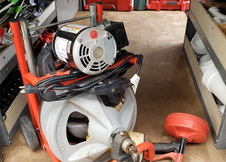 A plumbing snake machine with tools inside a utility trailer.