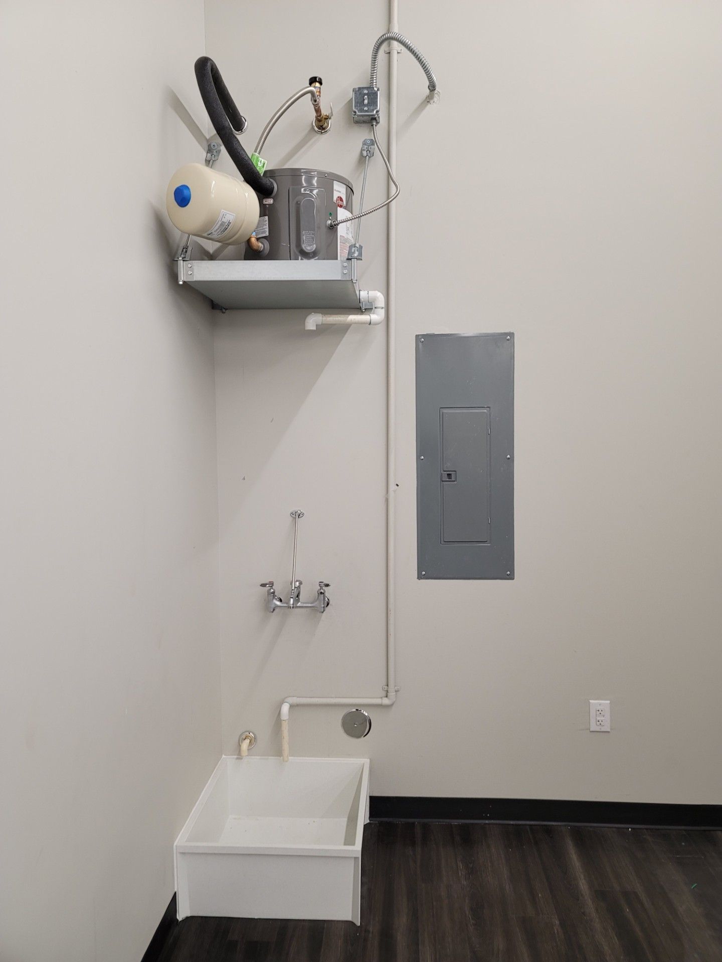 A utility room with a wall-mounted water heater, a sink, and electrical panel.