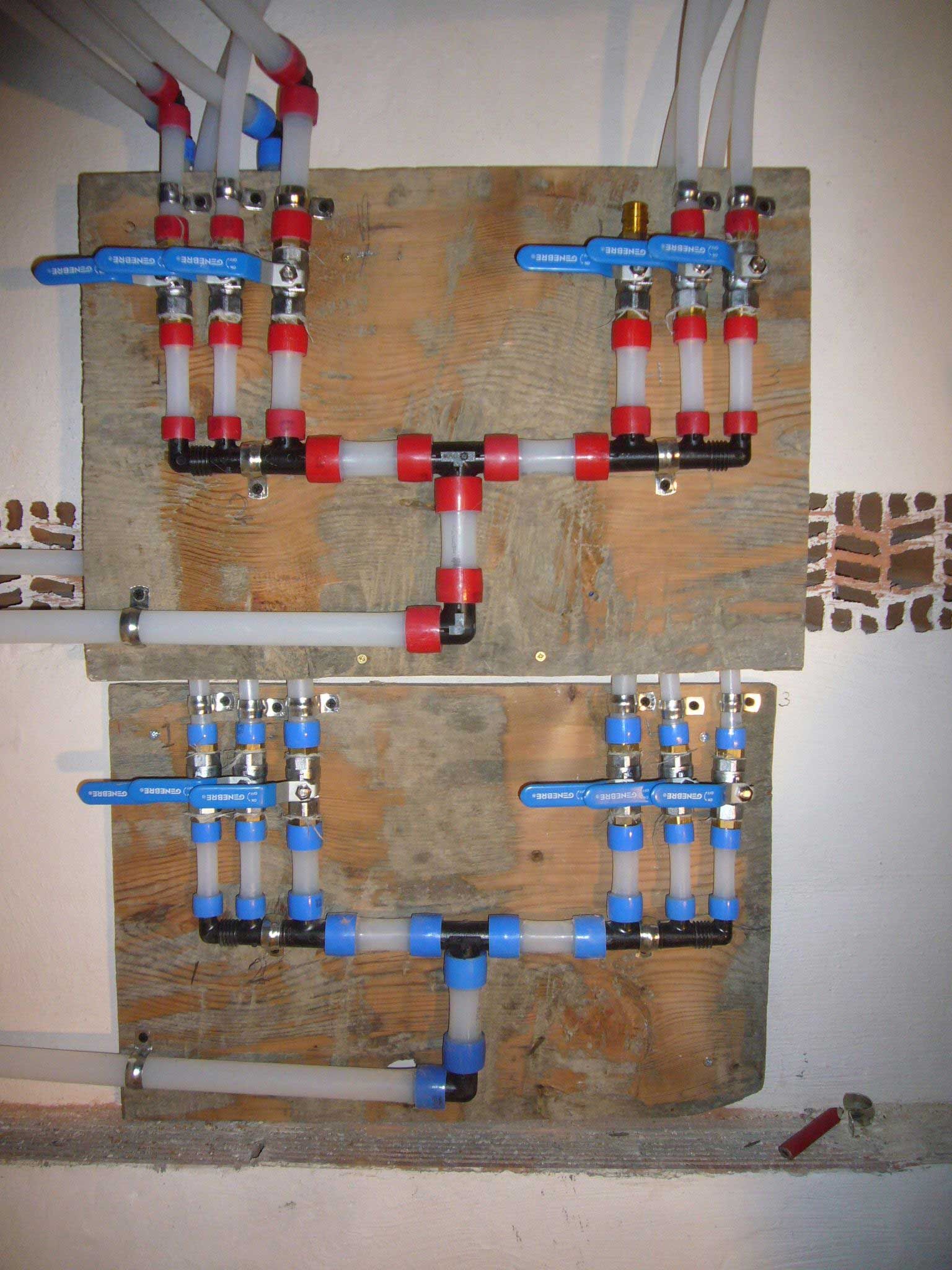 Piping system with red and black connectors, blue valves, and white tubes mounted on wood.