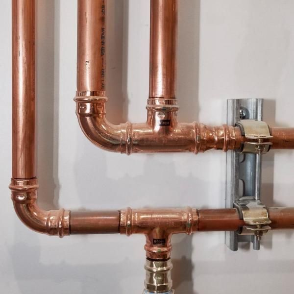 Copper pipes and fittings, secured with clamps, mounted on a white wall.
