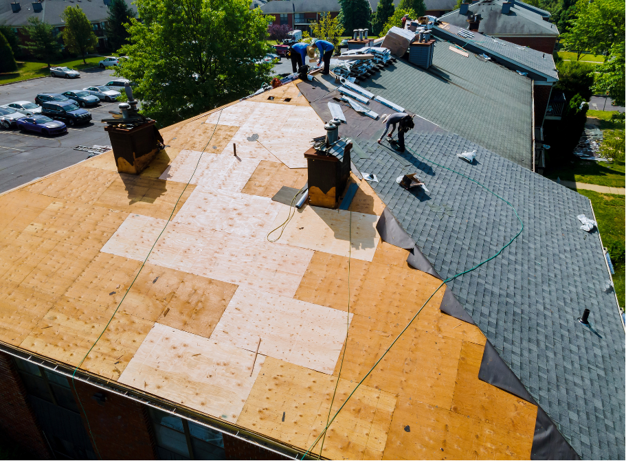 Roofing workers installing orange and gray shingles on a house roof during daytime