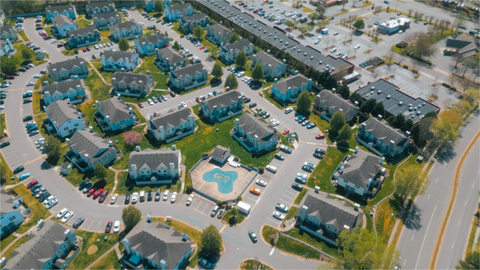 Aerial view of a suburban apartment complex with parking lots, trees, and nearby roads