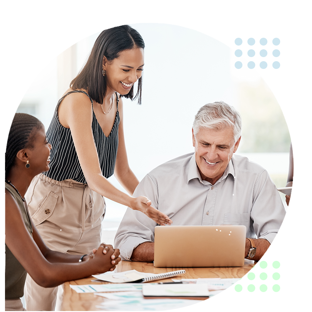 Three coworkers smiling around a laptop at a bright office table