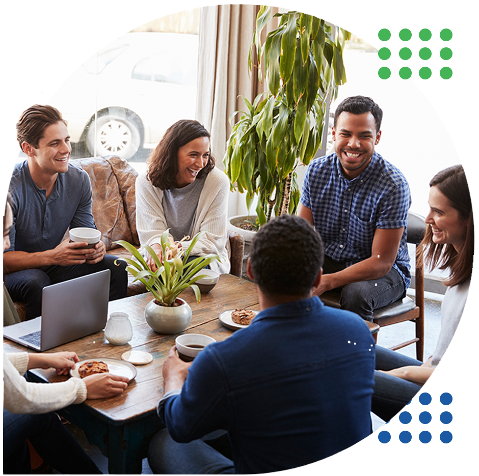 Team meeting around a table in a bright office, with laptops, coffee, and notes visible.