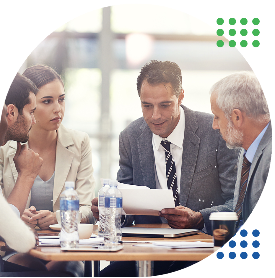 Business meeting with four people discussing documents around a conference table, with water bottles and coffee cups.