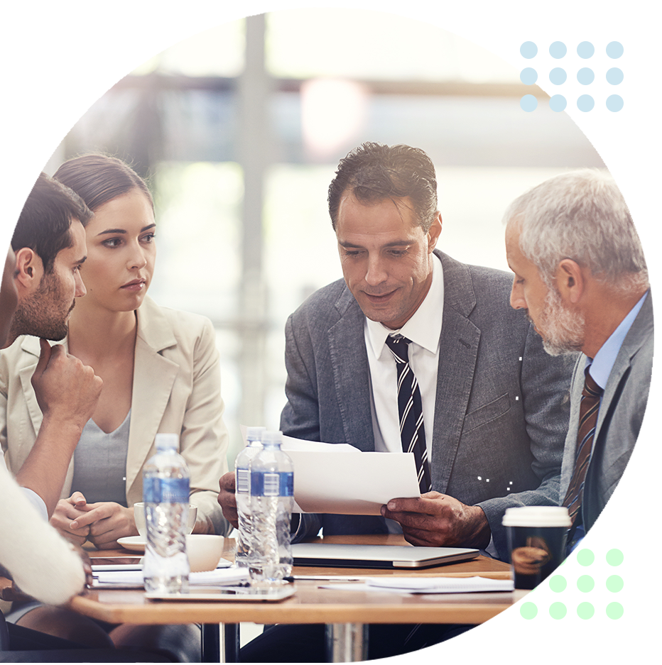 Four colleagues in a meeting reviewing documents around a conference table with coffee and water bottles