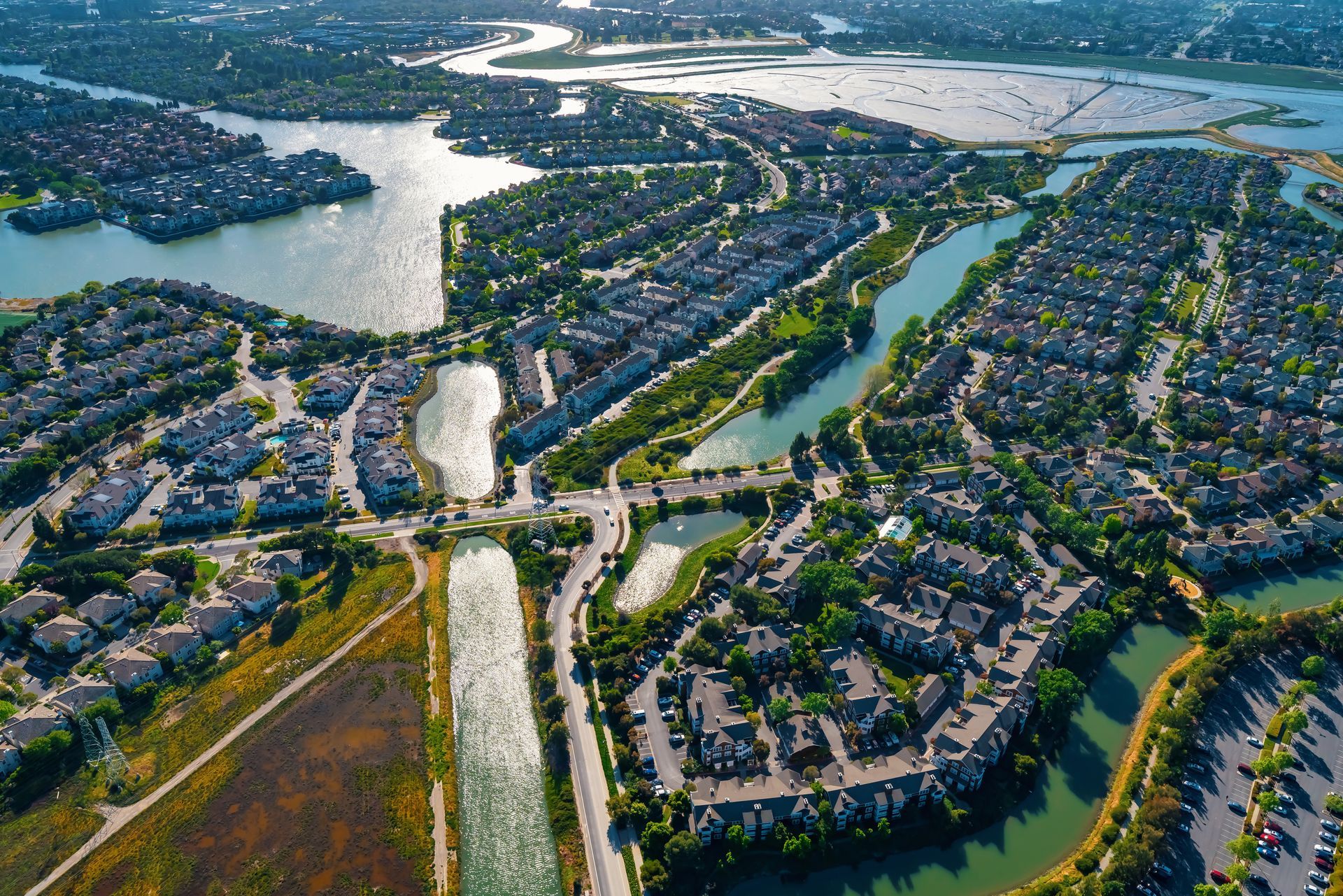 Aerial view of a suburban neighborhood with canals, roads, and a large lake in the background