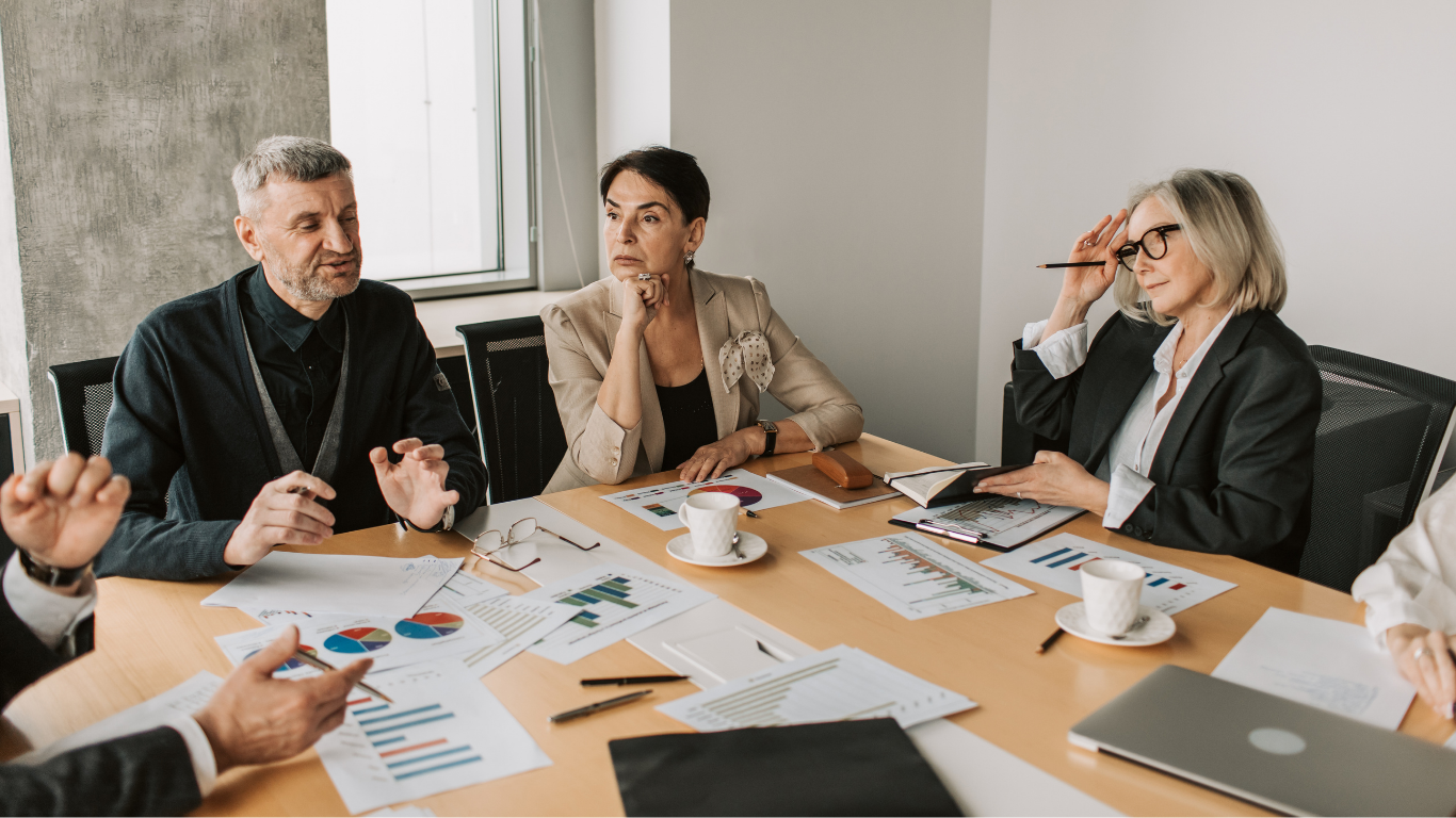 Three people in a meeting room discussing charts and documents around a table