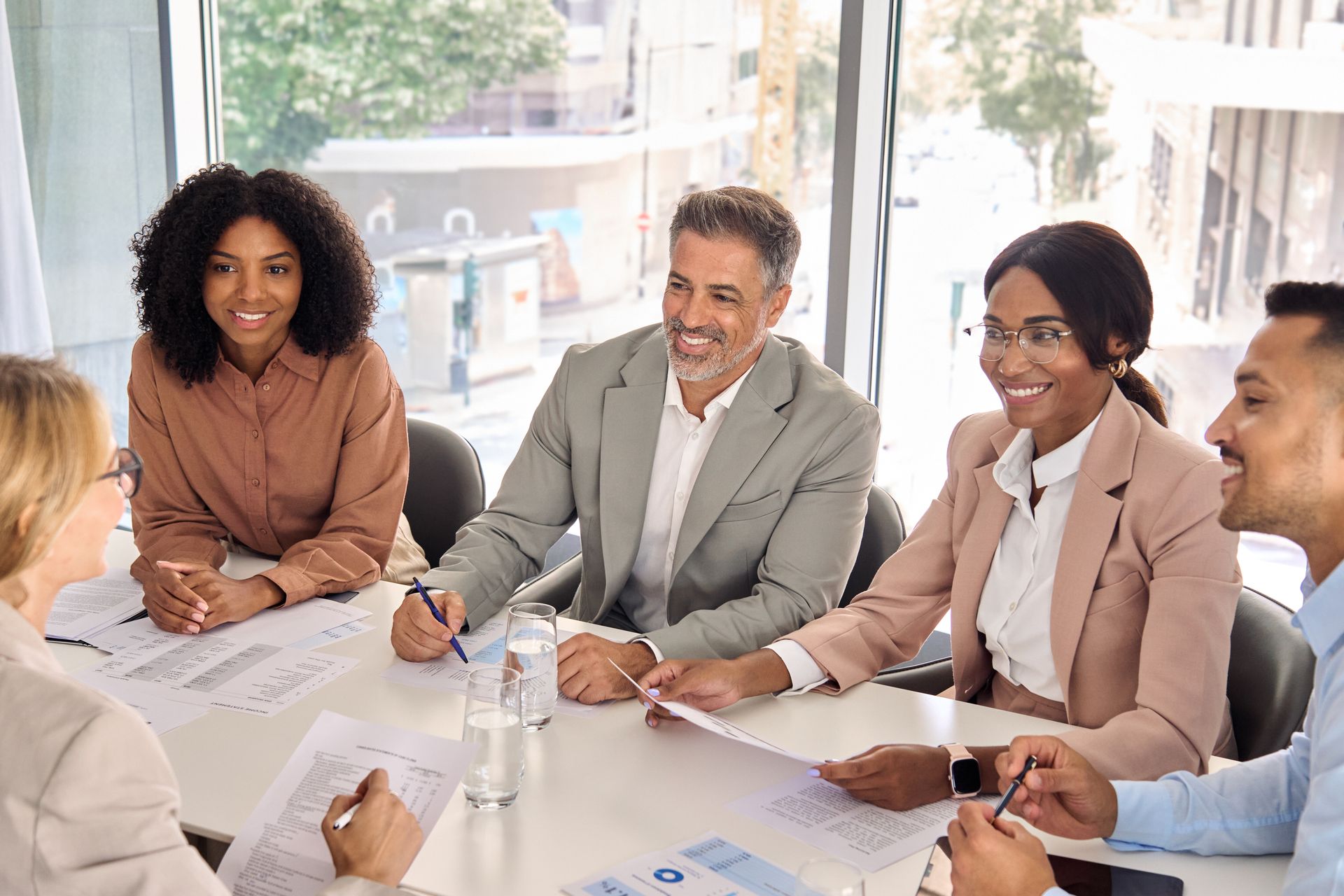 Team meeting around a table in a bright office, with notebooks, pens, and a laptop.
