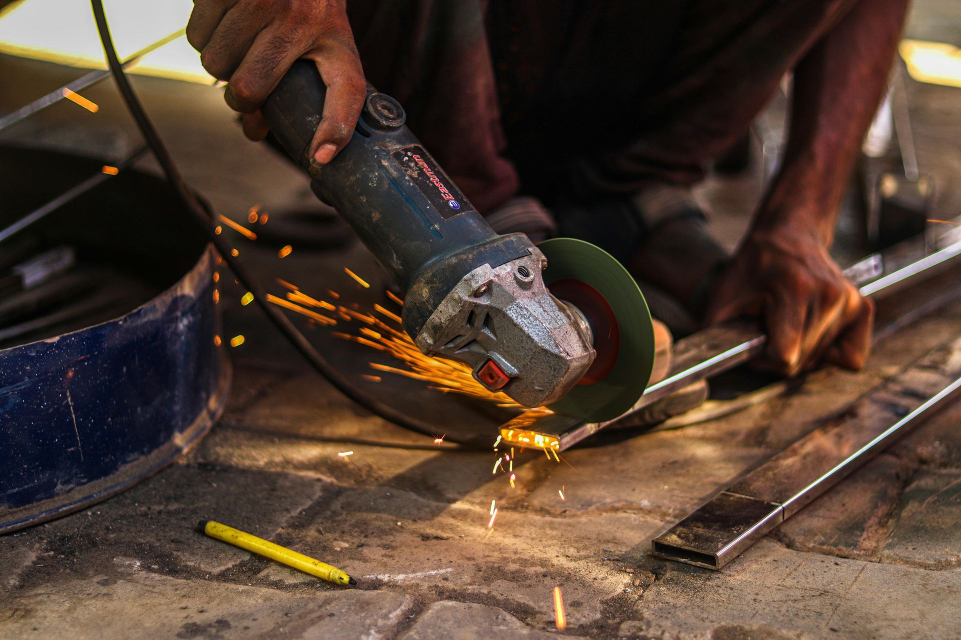 Person using an angle grinder on metal, with sparks flying in a workshop.