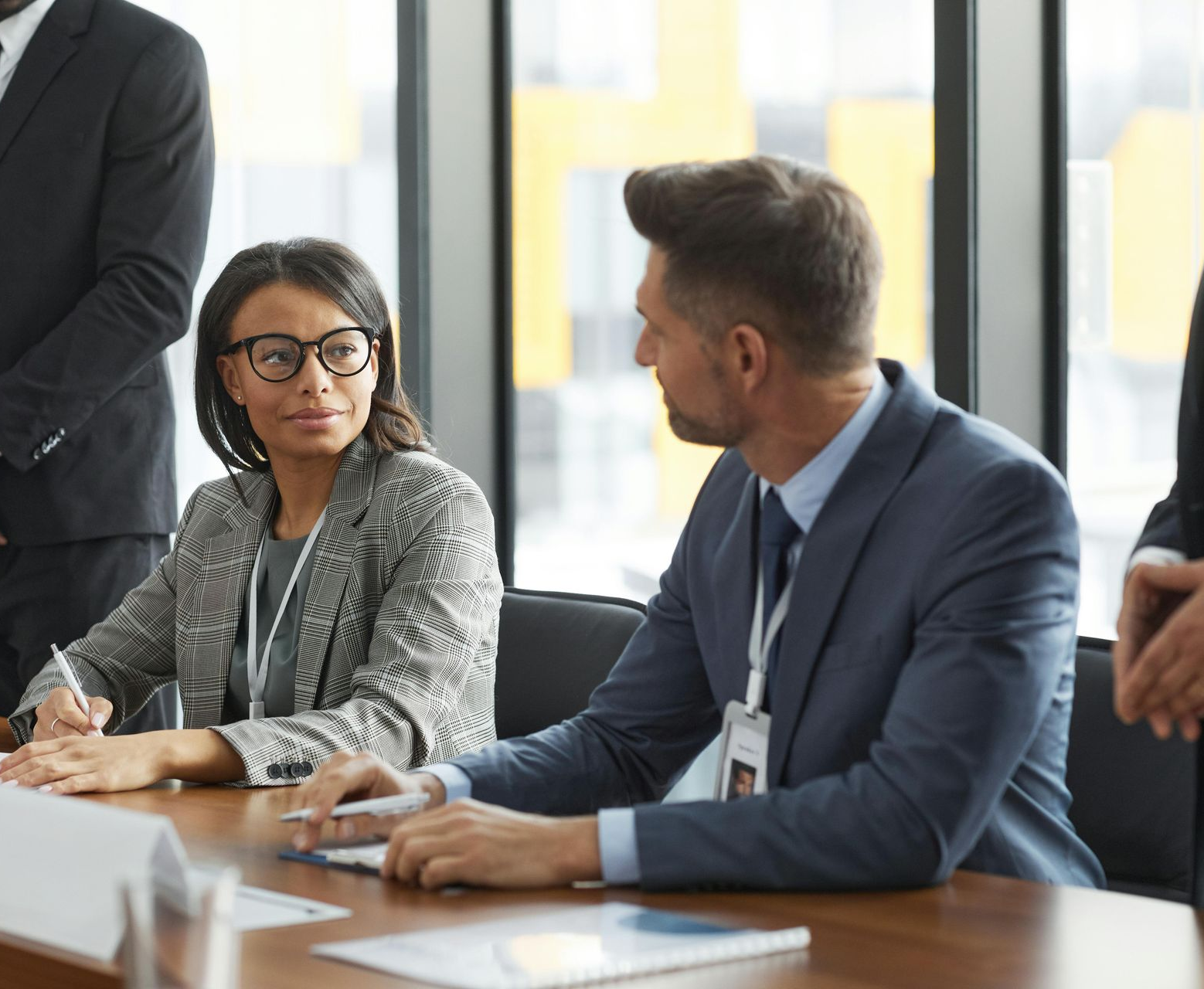 Two colleagues in a meeting room discussing at a conference table, with papers and laptops nearby.