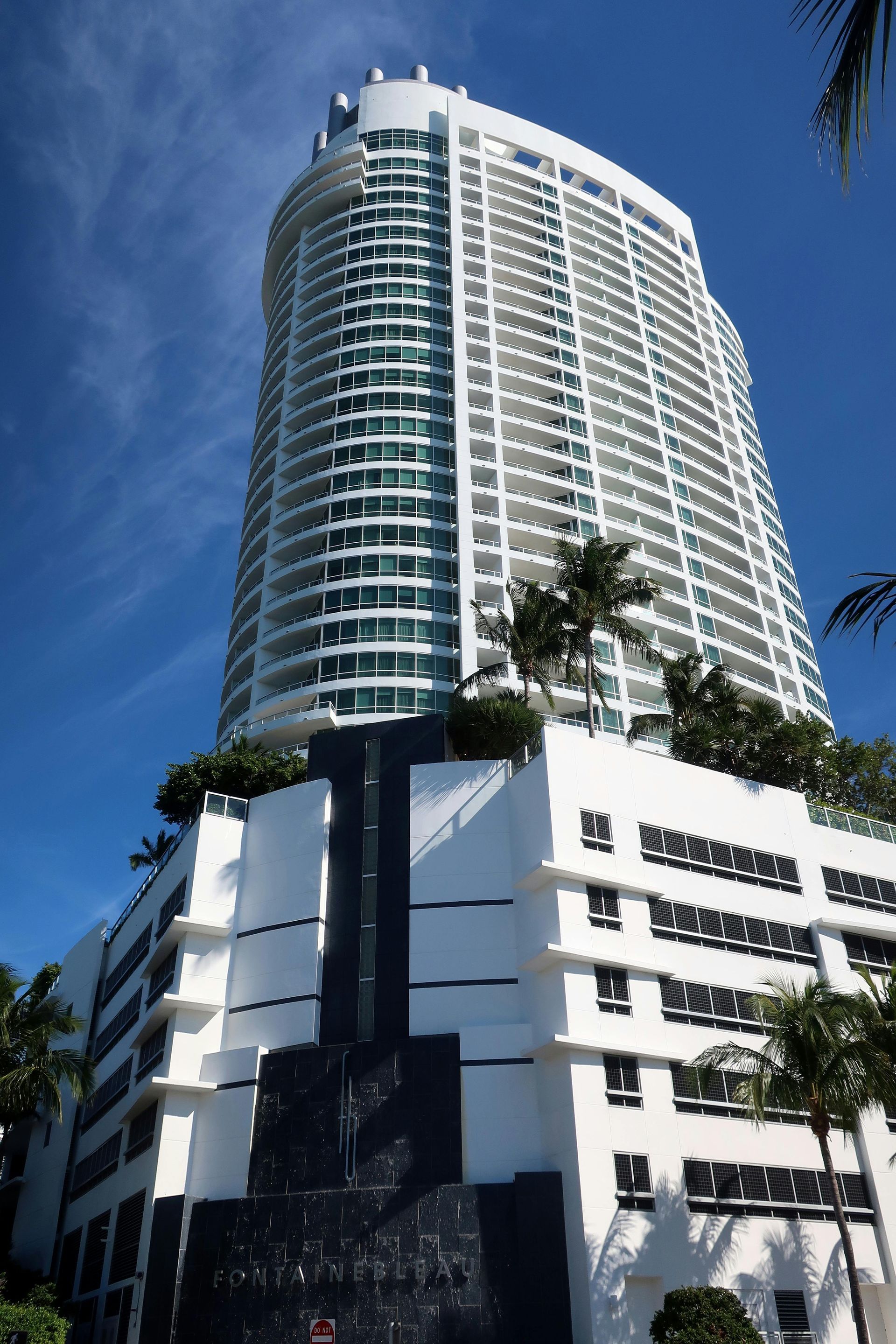 Tall modern white high-rise building with curved balconies against a blue sky
