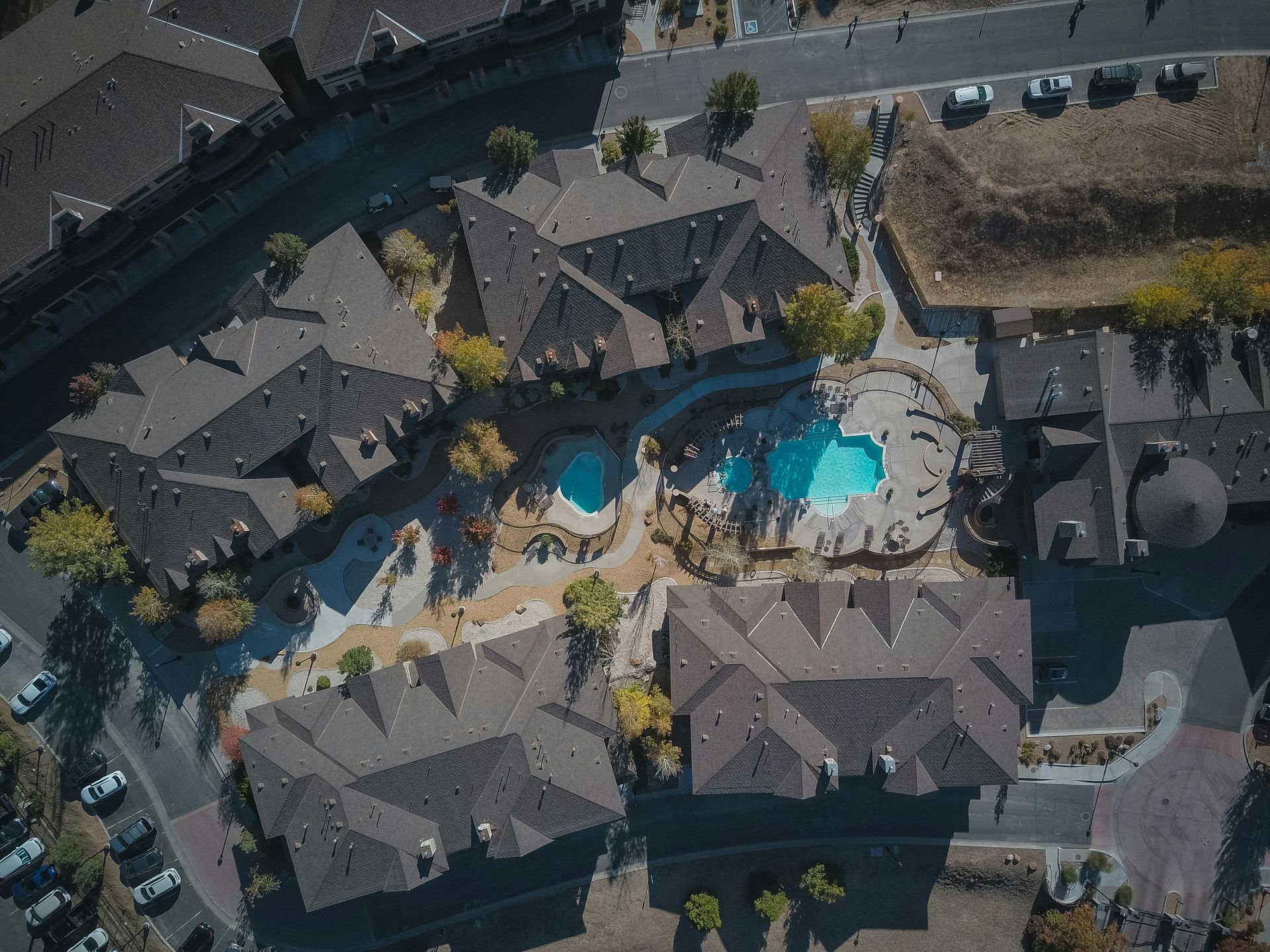 Aerial view of a resort with tiled-roof buildings and two blue swimming pools surrounding a central courtyard