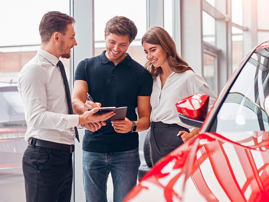 Um homem e uma mulher estão olhando para um tablet em uma sala de exposição de automóveis.