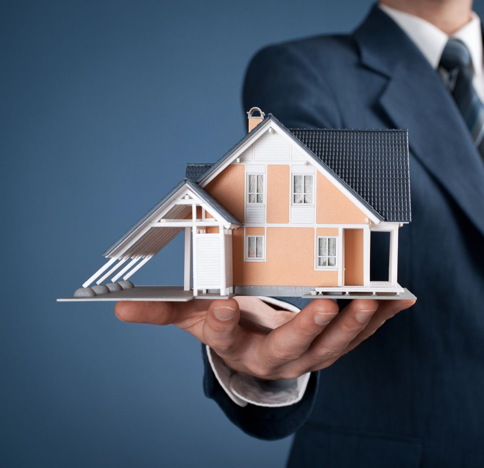 Uomo d'affari che tiene in mano un modellino di casa in miniatura su sfondo blu.