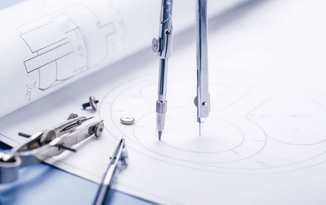 Strumenti di disegno tecnico: matita e compasso su una scrivania bianca.