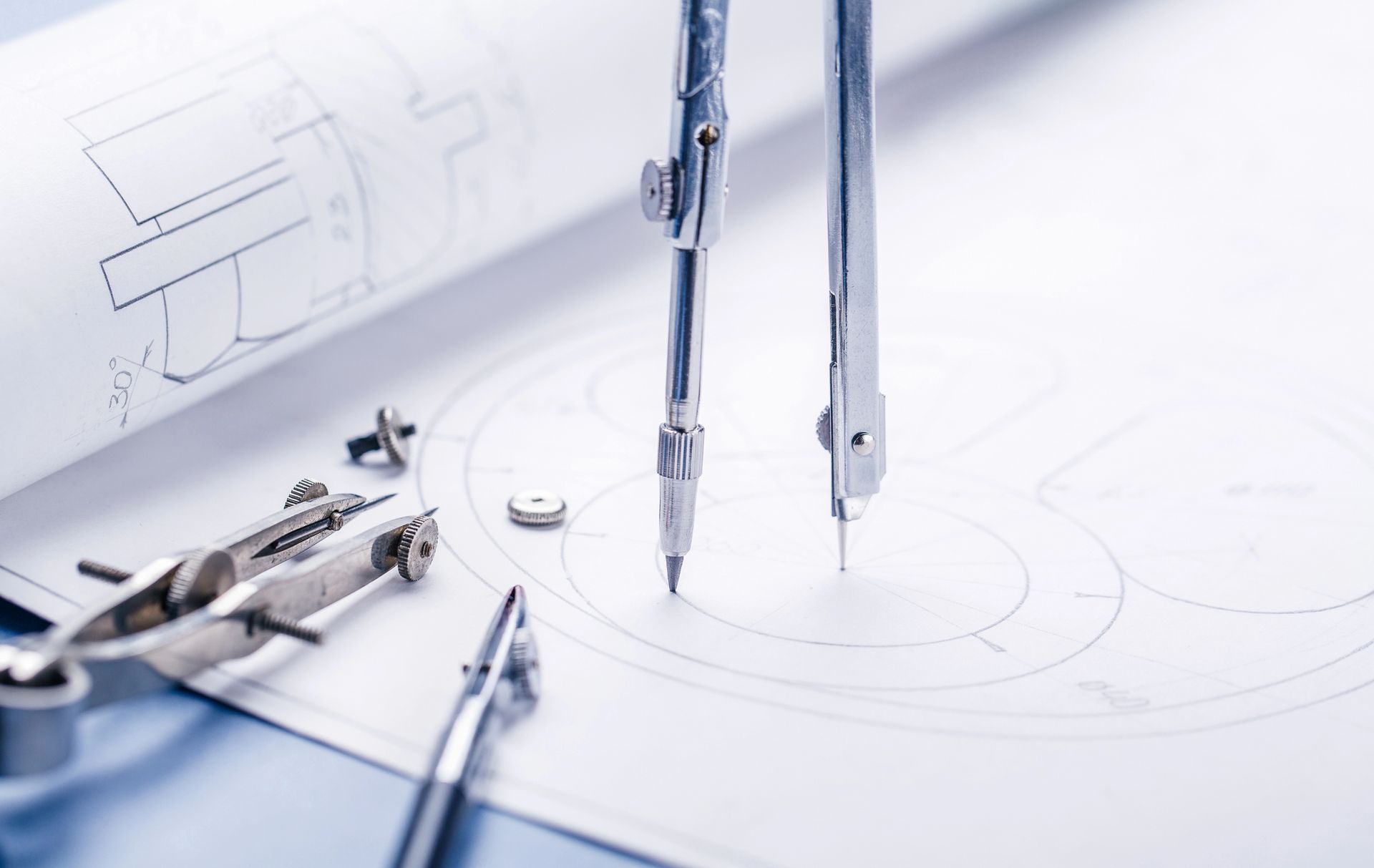 Strumenti da disegno e compasso su una superficie bianca da disegno tecnico, con planimetrie sullo sfondo.